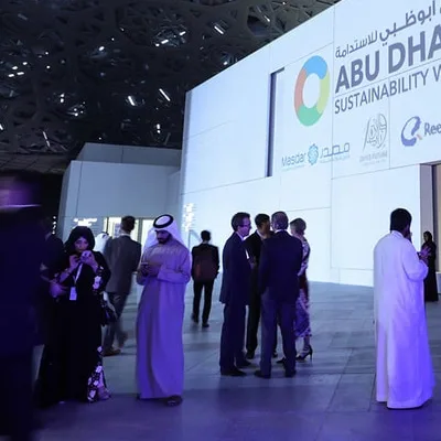 Conference and sustainability event environment with large presentation screens and attendees networking.