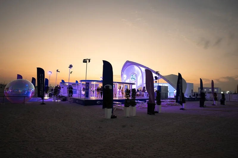 Outdoor event environment at sunset with temporary structures, lighting and visitor areas.