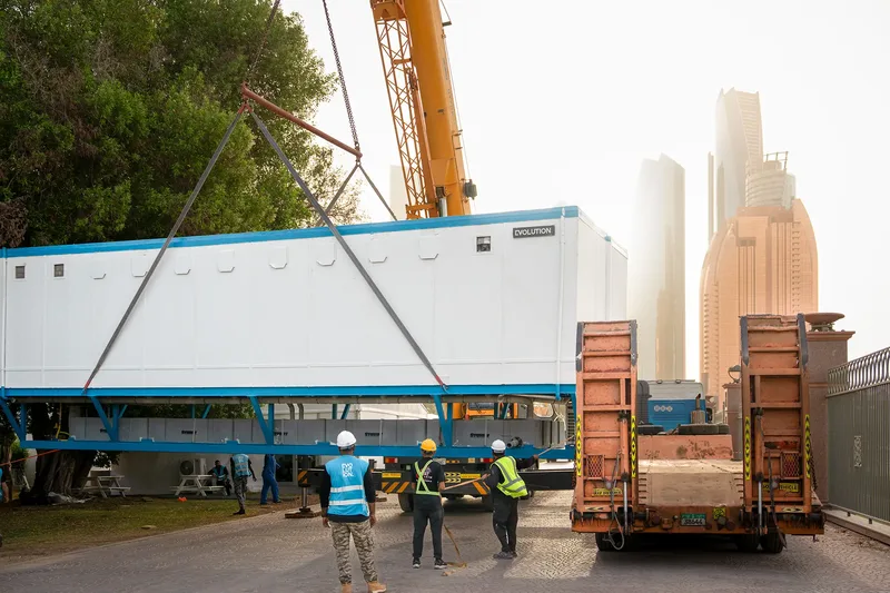 Temporary site cabin being installed by crane beside a delivery vehicle in Dubai.