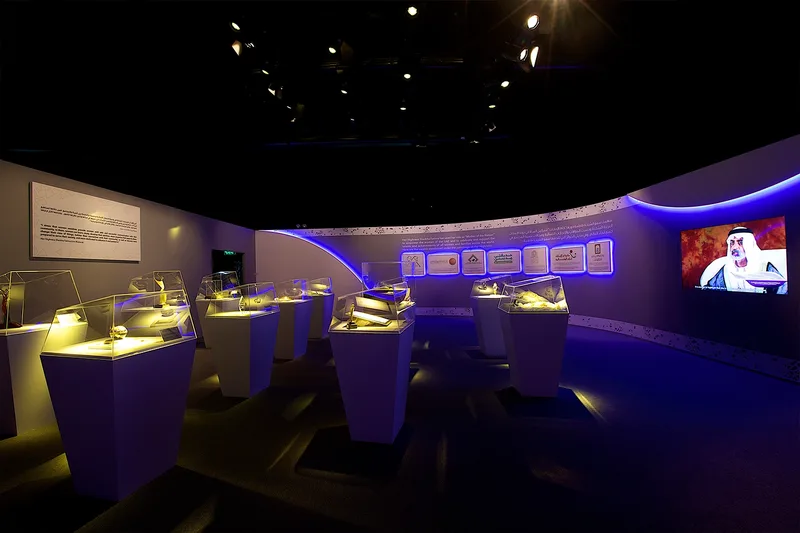 Immersive exhibition environment with illuminated display plinths, screens and curved feature walls.