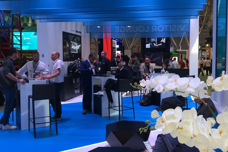 Busy exhibition hospitality area with bar seating, floral styling and branded displays.