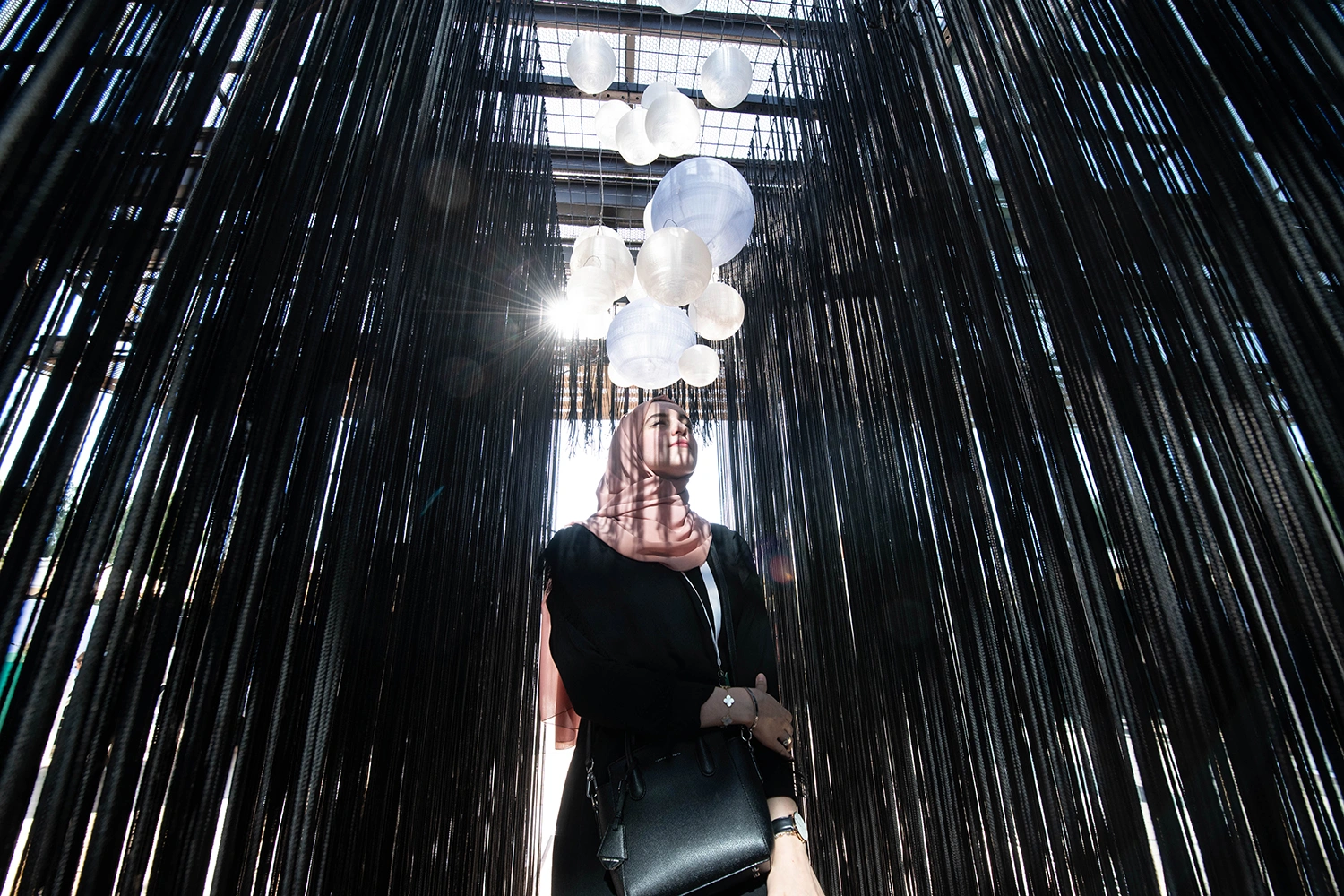 Visitor experiencing an immersive art installation at Al Burda Festival with suspended black strands and illuminated sculptural elements