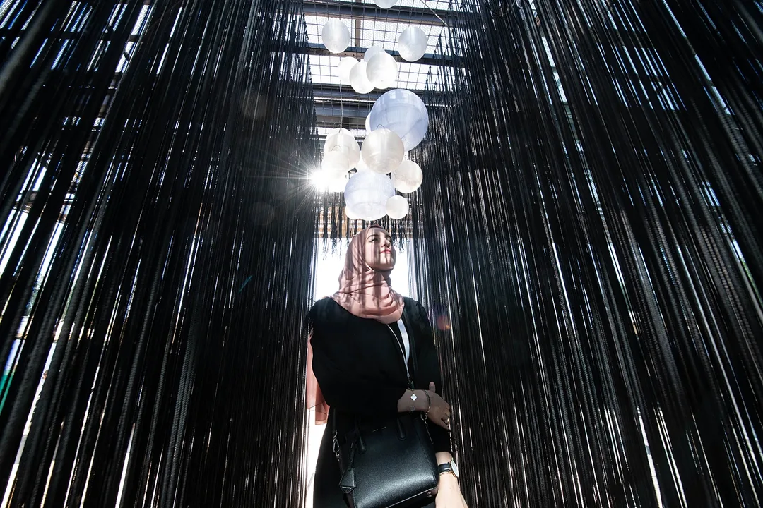 Visitor experiencing an immersive art installation at Al Burda Festival with suspended black strands and illuminated sculptural elements