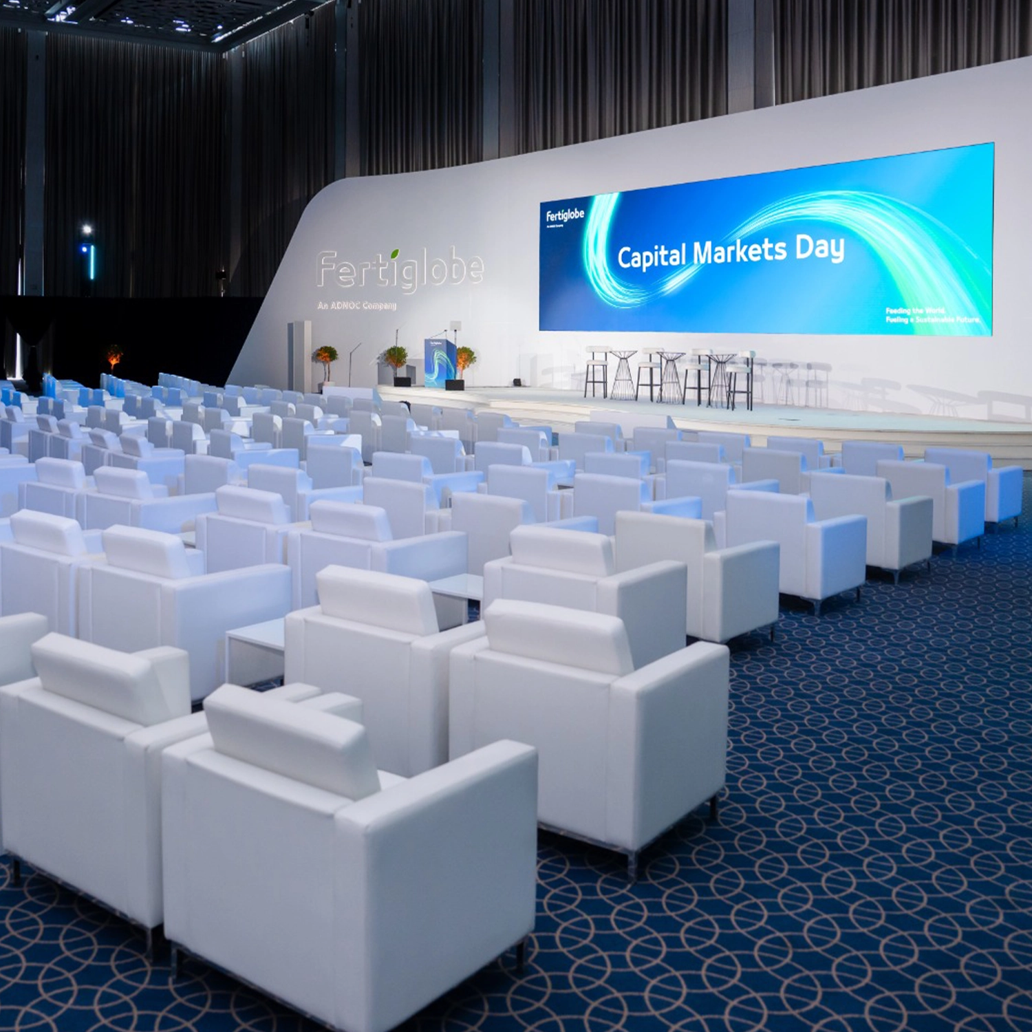 Capital Markets Day conference setup with branded stage, white lounge seating and presentation screen