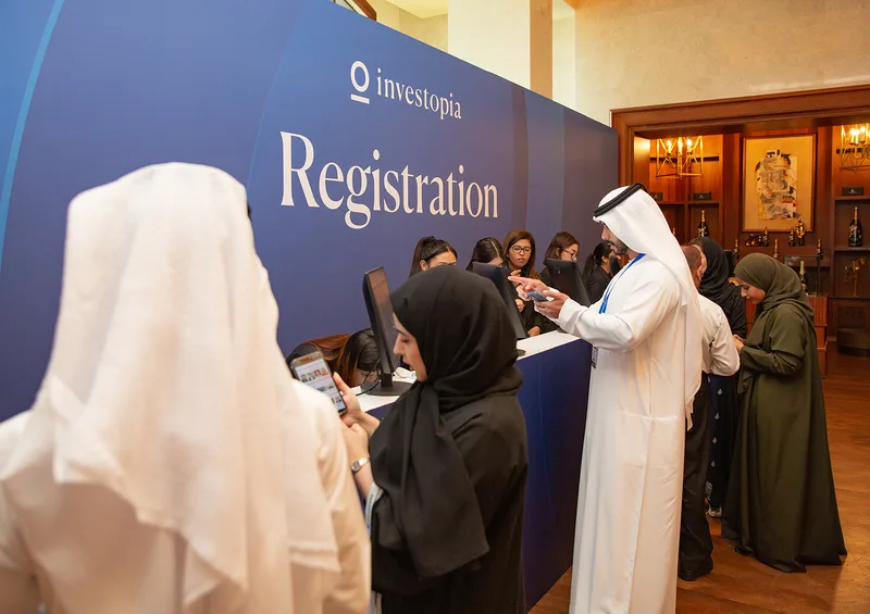 Investopia registration desk with branded backdrop, digital check-in screens and arriving delegates