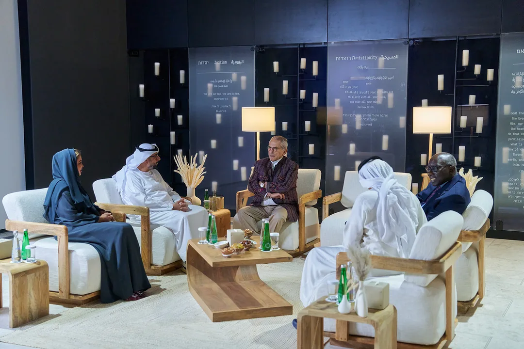 Human Fraternity Majlis in Abu Dhabi with senior guests seated in an interfaith discussion setting, hospitality furniture and multilingual cultural displays