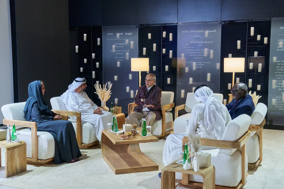 Human Fraternity Majlis in Abu Dhabi with senior guests seated in an interfaith discussion setting, hospitality furniture and multilingual cultural displays