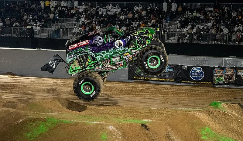 Grave Digger monster truck performing a jump at Monster Jam Liwa with temporary arena, grandstands and live audience