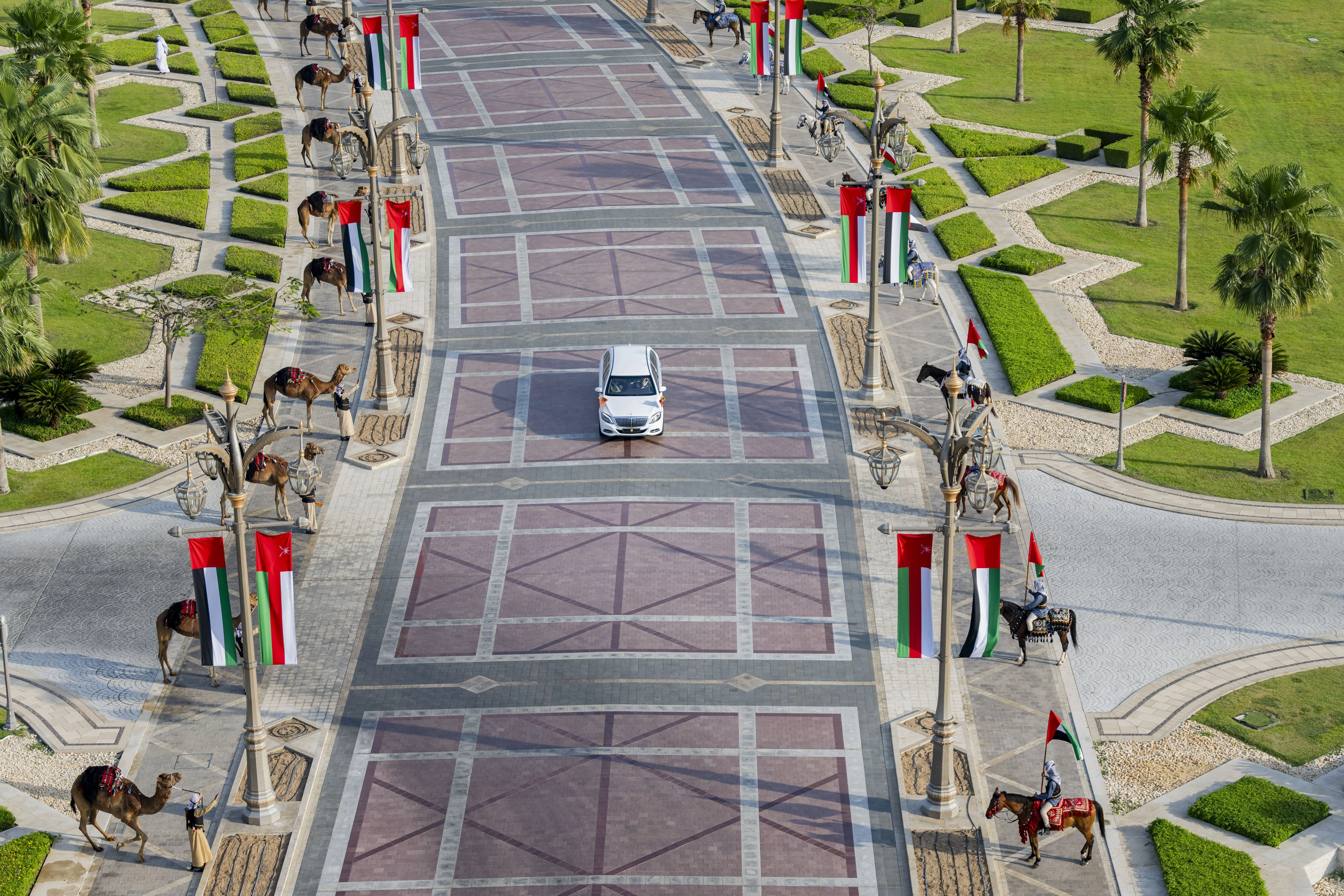 Official Oman state reception motorcade route in Abu Dhabi with ceremonial camels, mounted riders and UAE flags