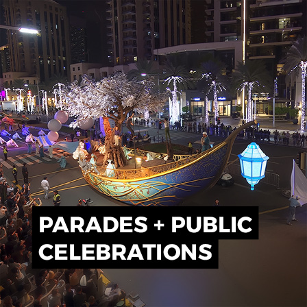 Large public celebration with illuminated parade float, performers and crowds in an outdoor event setting