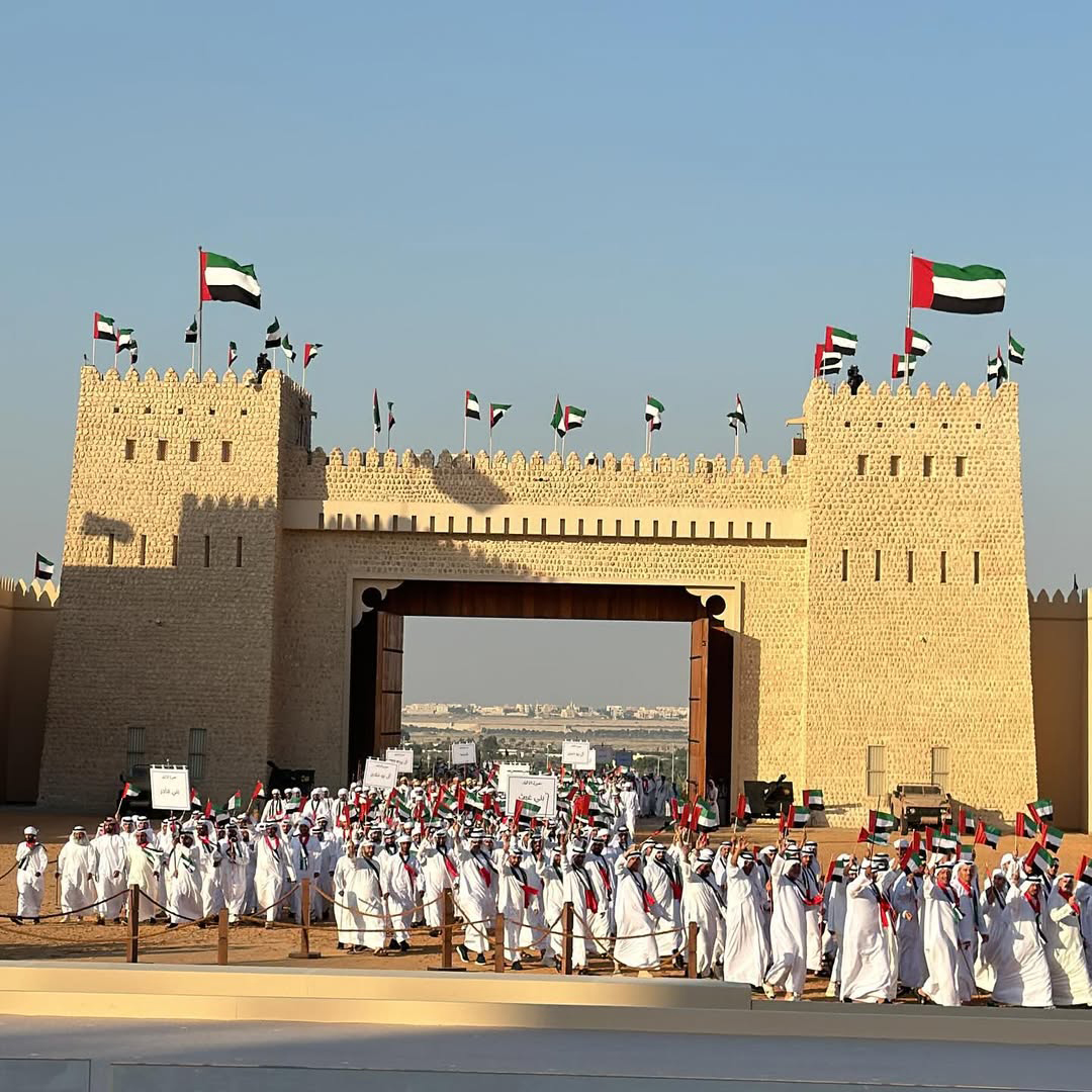 Large Union Parade 2025 procession entering through a traditional fort gate in Abu Dhabi with crowds waving UAE flags