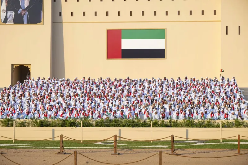 Large formation of Union Parade 2025 participants in traditional dress beneath a giant UAE flag backdrop