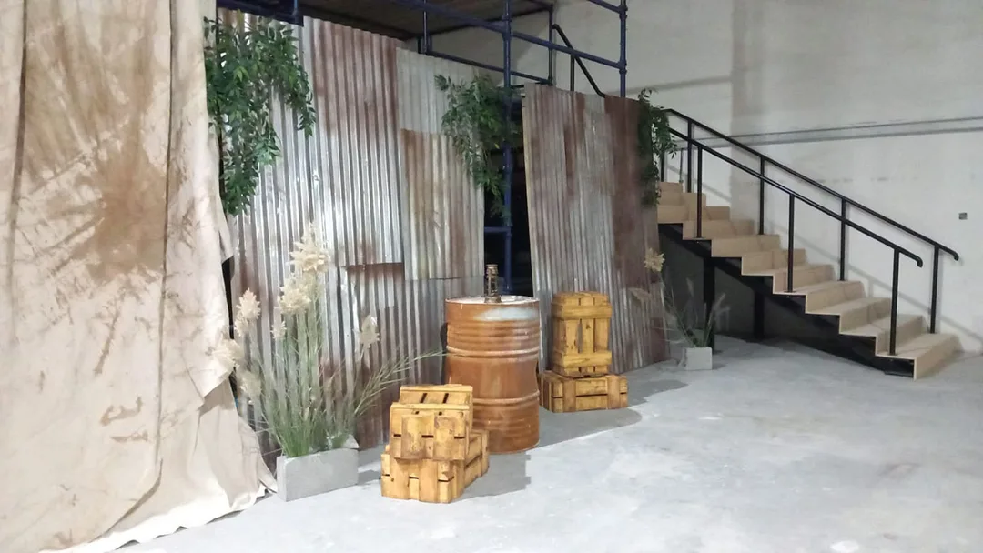 Weathered corrugated entrance panels and distressed oil drum styling for The Last of Us