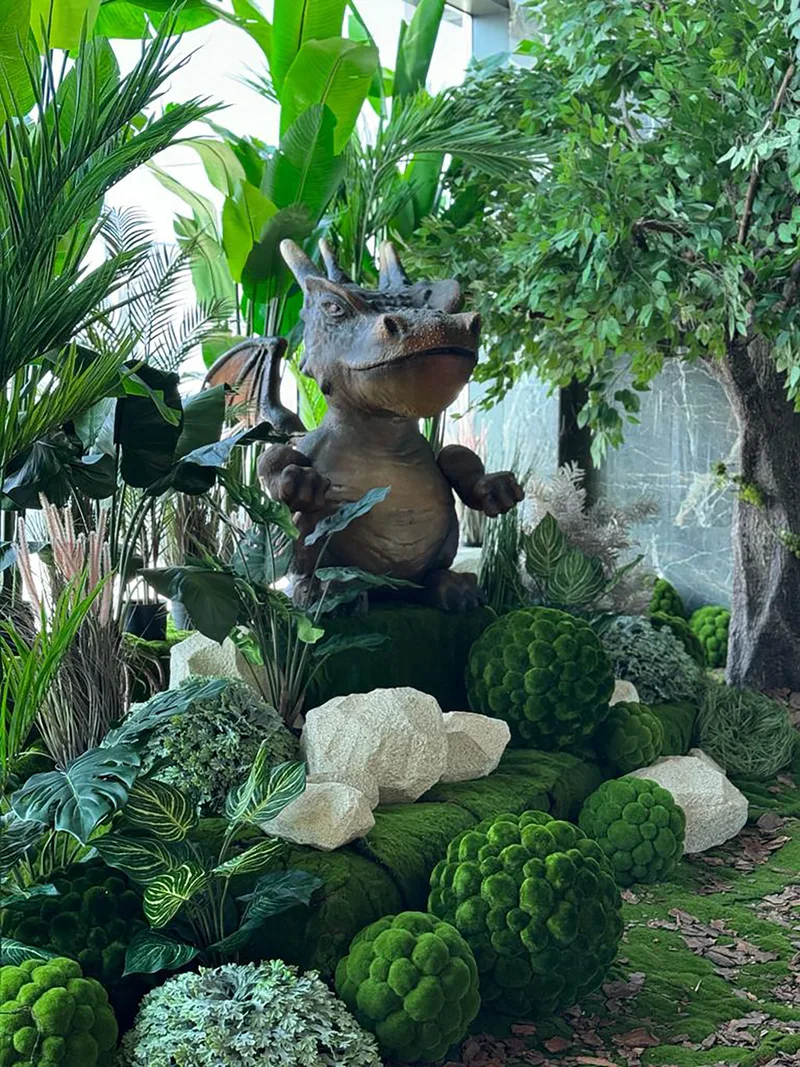 Giant fantasy dragon prop surrounded by moss, decorative rocks and tropical foliage at EINO.