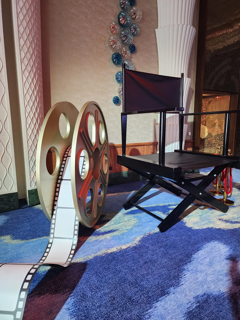 Hollywood director's chair displayed alongside an oversized decorative film reel and illuminated filmstrip.