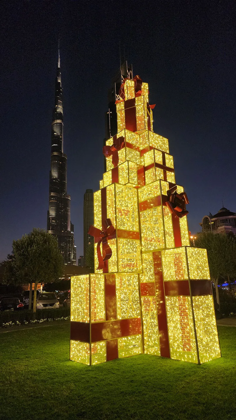Warm LED gift box props stacked into a towering festive statement installation