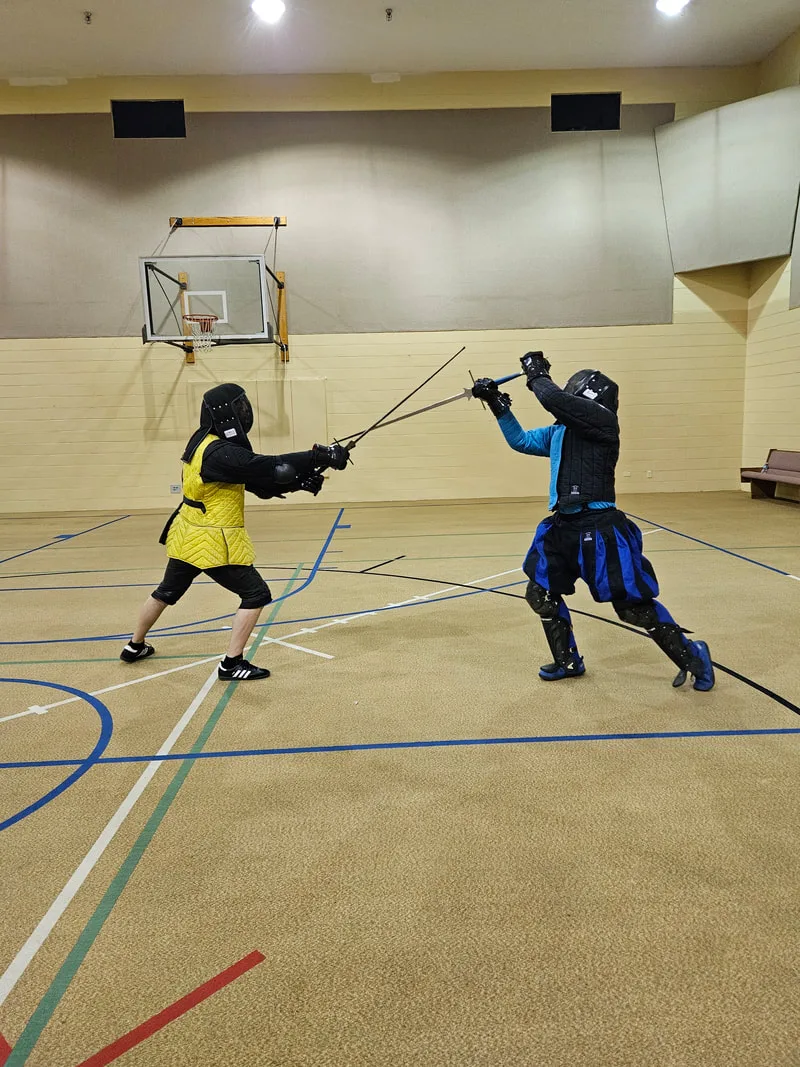 Instructor Ryan and an adult student engaged in a longsword fight.