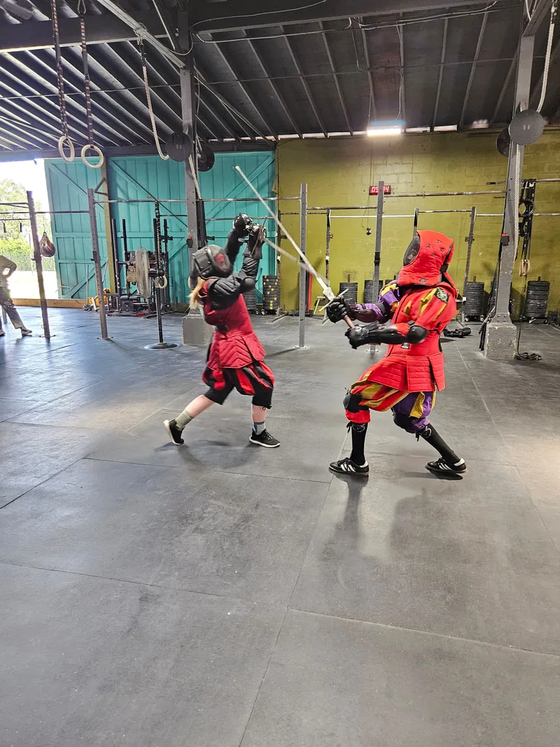 Teen students Alyx and Galloway sparring with longswords.