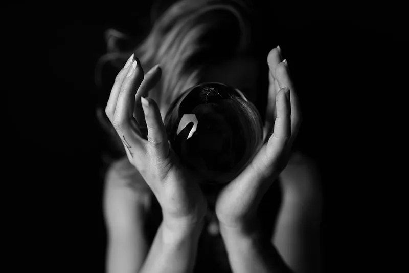 Photographie d'art sombre en noir et blanc mettant en scène une femme avec une boule de cristal