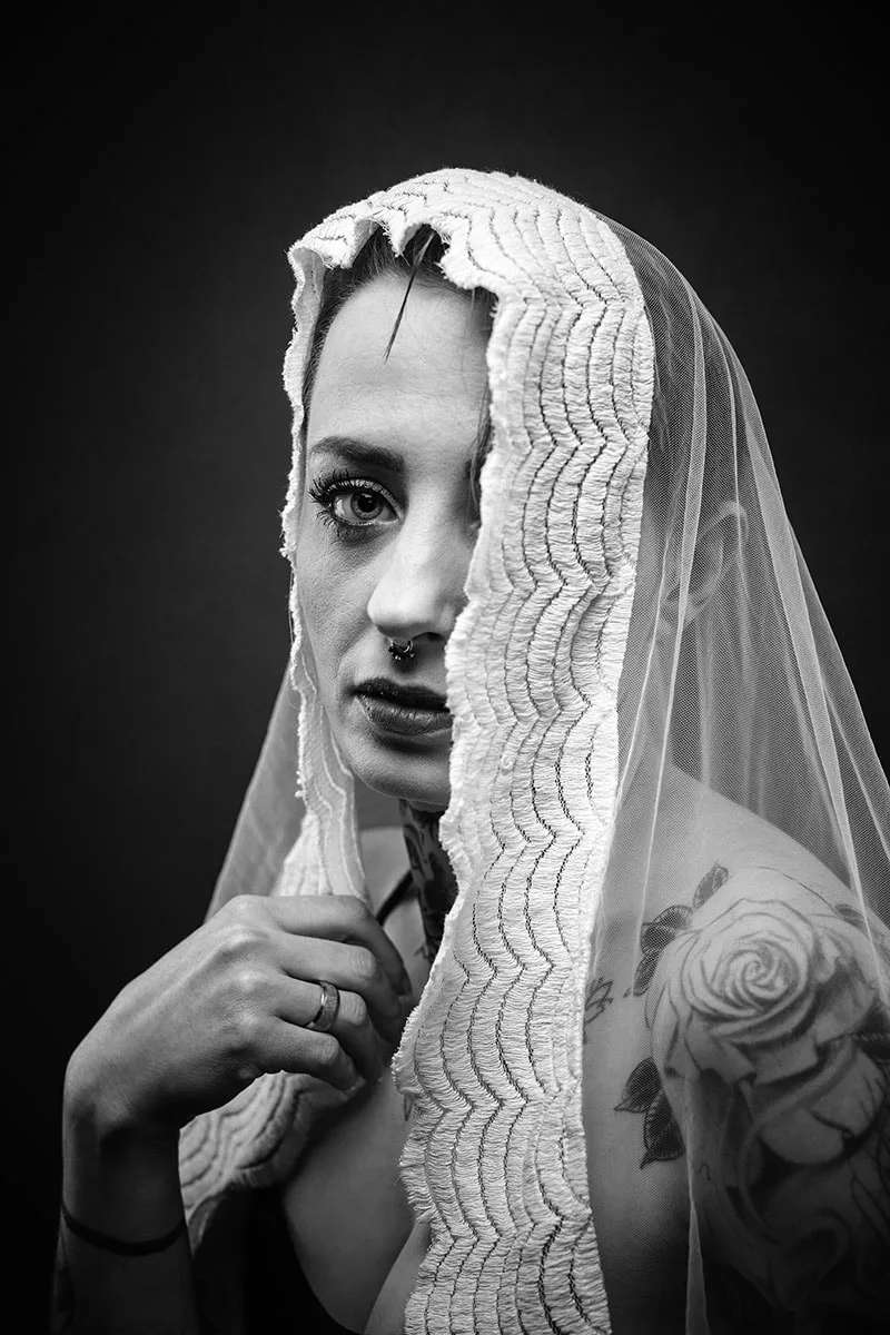 Portrait artistique d'une femme au regard doux voilée d'un tissu transparent laissant deviner ses tatouages