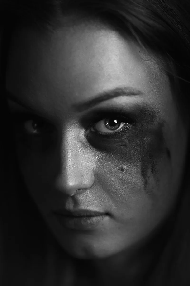 Portrait low-key à fort contraste montrant un regard intense et des larmes de maquillage