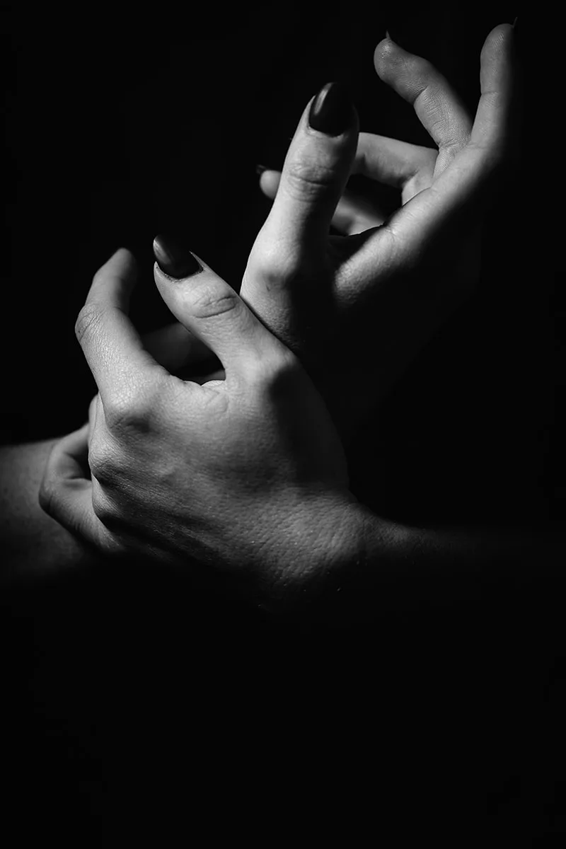 Composition en clair-obscur mettant en valeur les ombres et les textures sur les mains d'une femme