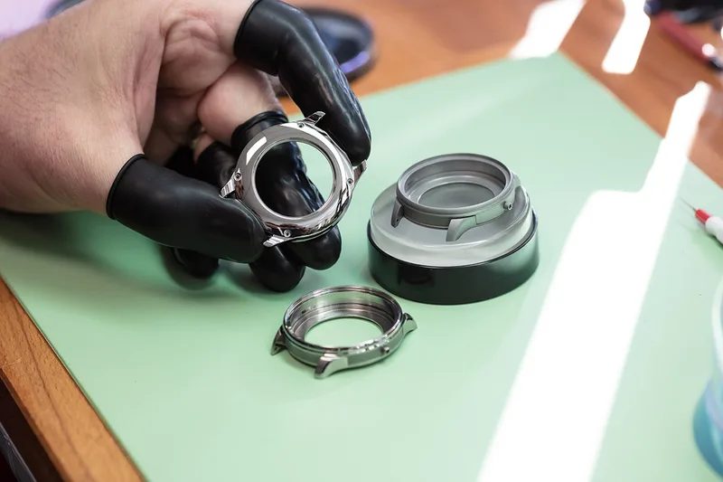 Boîtier de montre manipulé avec des gants dans un atelier horloger