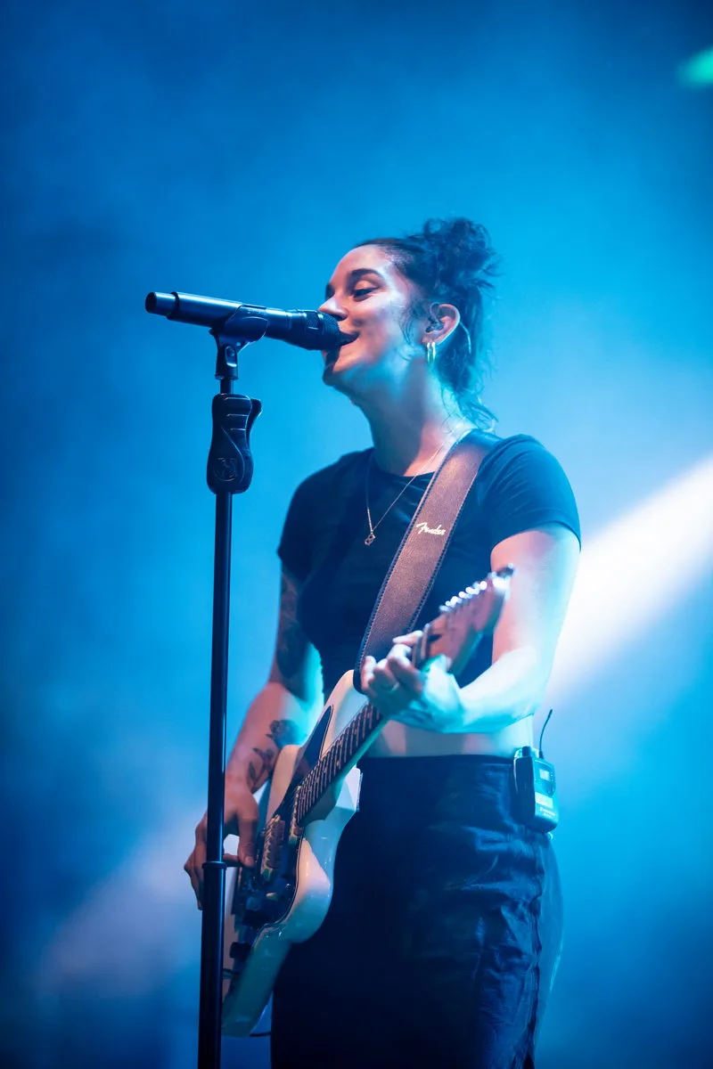 amille Contreras, chanteuse de Novelists au micro avec sa guitare dans une ambiance scénique bleue