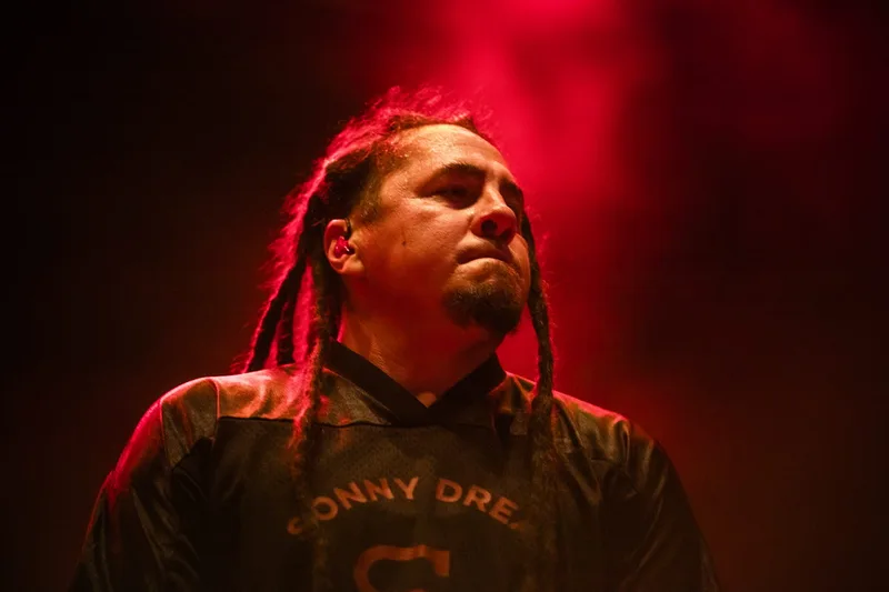 Sonny Sandoval, leader de P.O.D, sur scène dans une atmosphère de concert rouge et contrastée