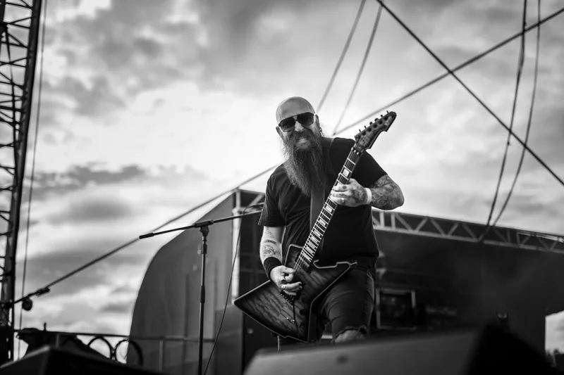 Le guitariste du groupe Cage Fight performant en plein air sous un ciel nuageux en noir et blanc