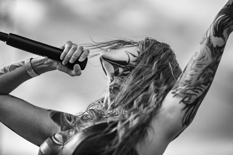 Rachel Aspe, chanteuse de Cage Fight, hurlant dans son micro sous un ciel nuageux dramatique