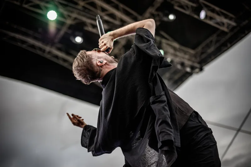 Max Rodriguez-Medallo, chanteur du groupe Revnoir en pleine action scénique sur fond de ciel nuageux