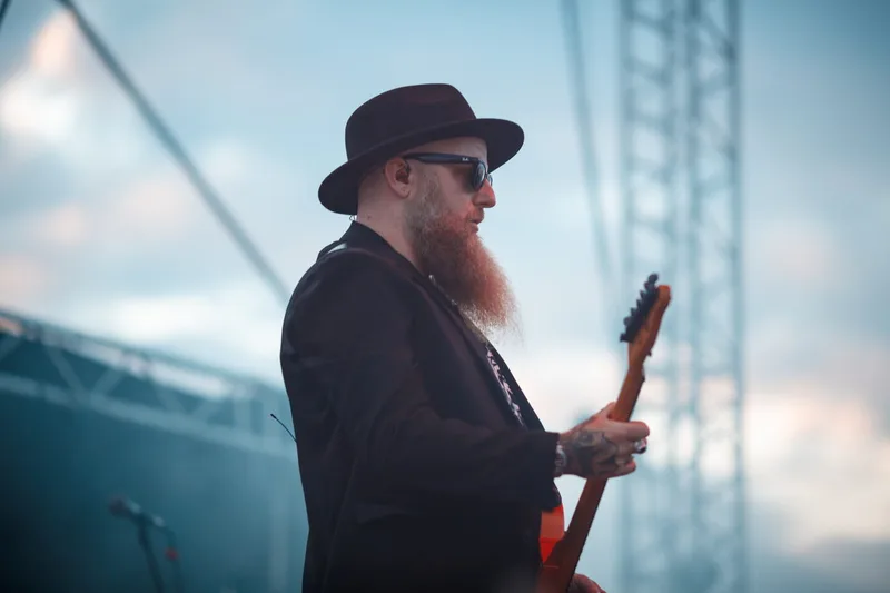 Le guitariste de Skindred jouant de son instrument sous les jeux de lumières bleues d'une scène de festival