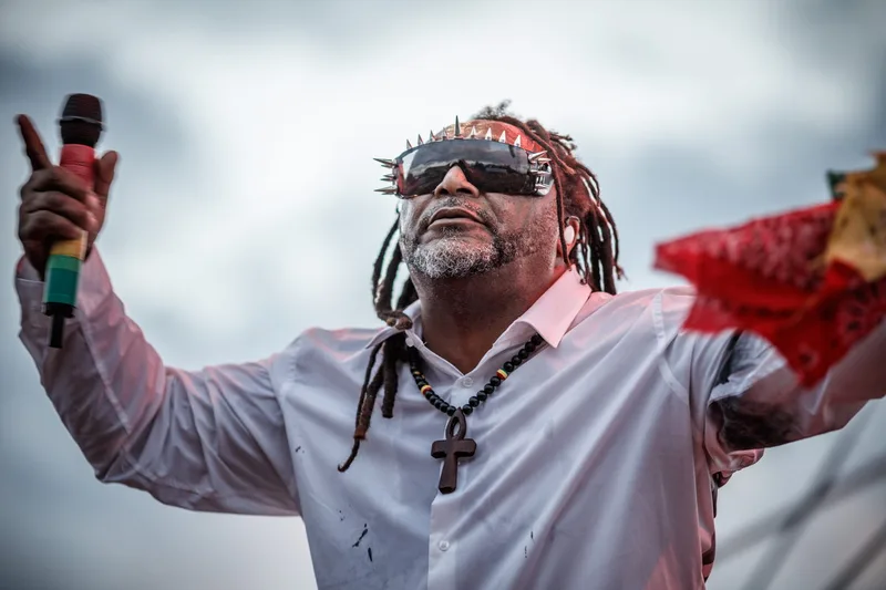 Benji Webbe, chanteur de Skindred, portant ses lunettes emblématiques sur scène en extérieur