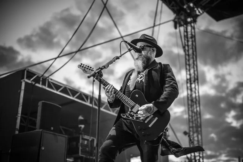 Le guitariste de Skindred jouant un accord sous un ciel nuageux capturé en noir et blanc