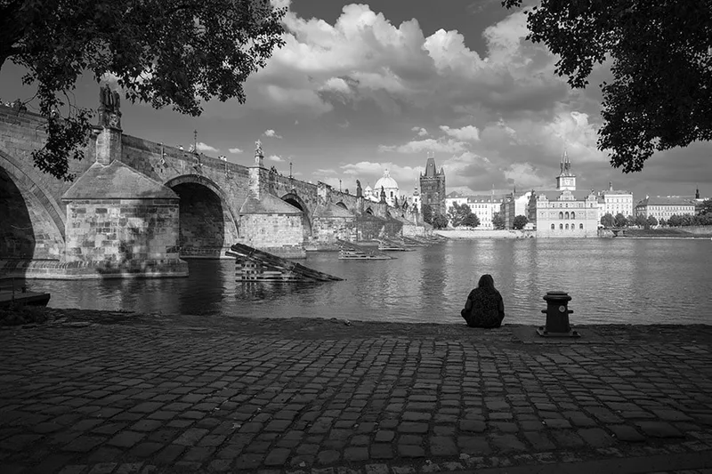 Silhouettes solitaires sur le pont Charles à Prague en noir et blanc sous un ciel nuageux