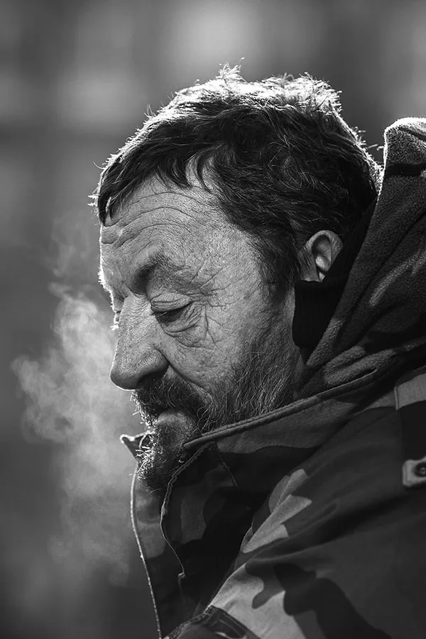 Portrait humaniste de profil d'un homme sans-abri aux rides marquées, entouré de fumée