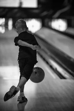 Photographie sur le vif en noir et blanc d'un enfant au bowling, illustrant la capture de l'instant décisif