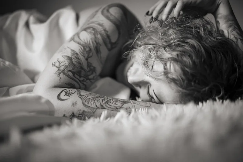 Photo intimiste en lumière naturelle mettant en valeur la complicité, le rire et les tatouages d'une femme