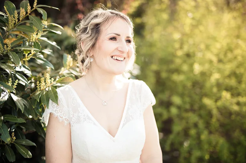 Sourire lumineux de la mariée au cœur de la verdure lors de la séance de couple