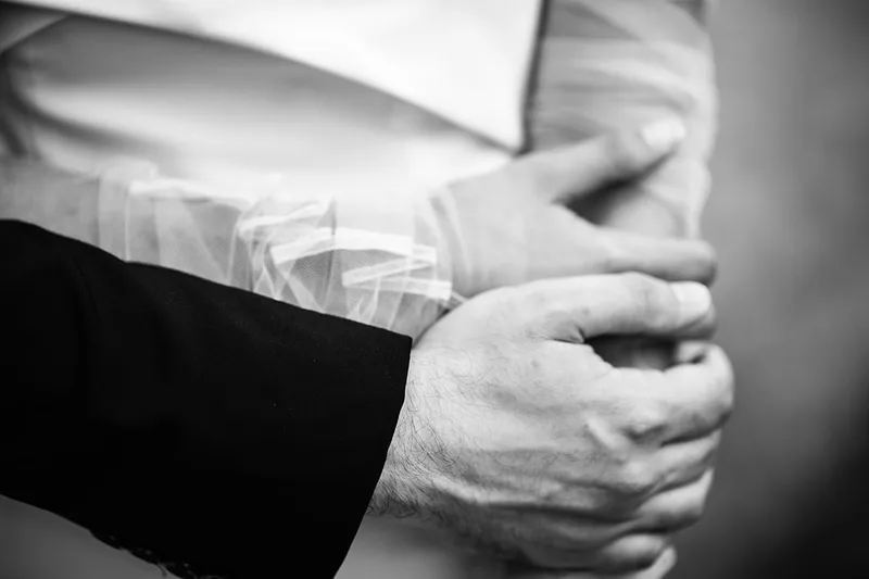 Gros plan poétique en noir et blanc sur les mains unies des mariés exprimant la tendresse