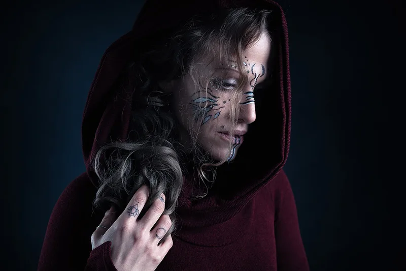 Portrait artistique d'une femme encapuchonnée avec maquillage graphique, ambiance sombre