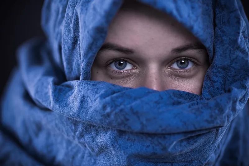Portrait artistique d'une femme au regard bleu, visage enveloppé dans un tissu