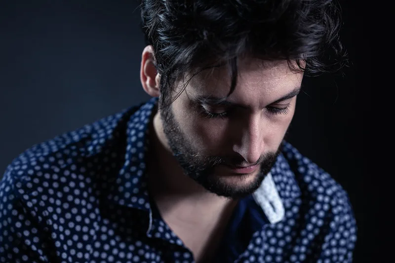 Portrait artistique en couleur d'un homme barbu, lumière douce et regard baissé