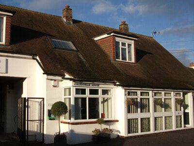 Exterior view of Surrey Injury Clinic, Caledonian House in Horley, featuring white brickwork and a clear sign. The entrance is welcoming and well-lit.