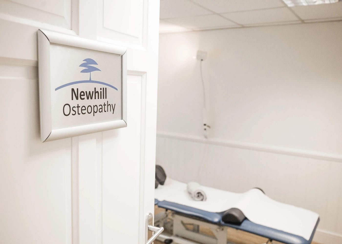 Open door with Newhill Osteopathy sign on it, leading to a treatment room.