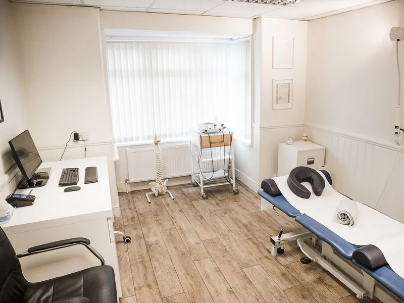 A bright, modern osteopathy treatment room at Newhill Osteopathy at the Surrey Injury Clinic, Reigate Road, Horely with a blue clinical plinth, anatomical spine model, and professional diagnostic equipment.