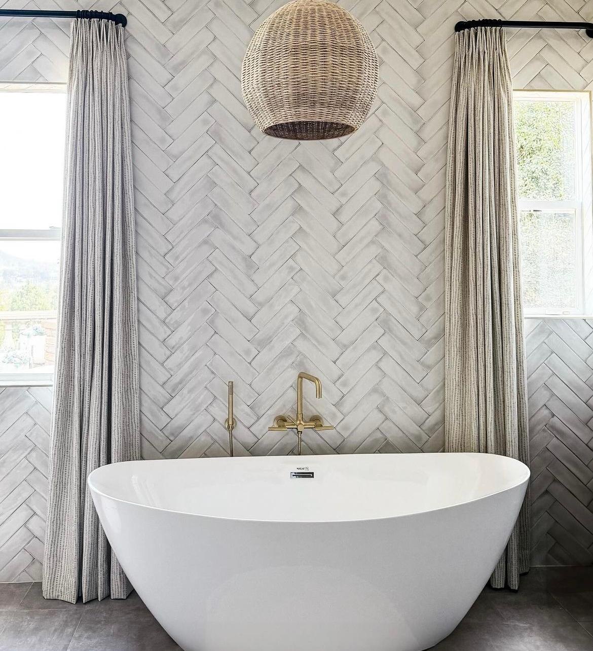 Primary bathroom freestanding tub with a rattan pendant and herringbone tile wall by Jill Seidner Interior Design