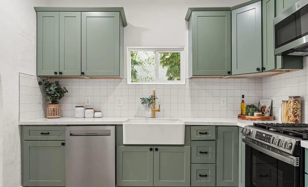 Sage green kitchen with a farmhouse sink under the window by Jill Seidner Interior Design