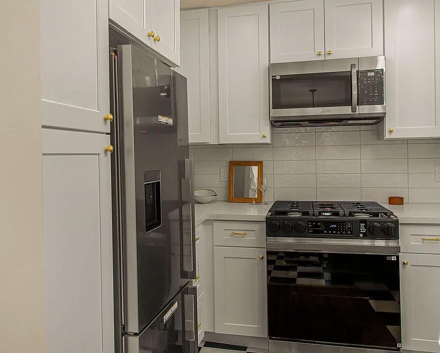White kitchen with a stainless refrigerator and a black range by Jill Seidner Interior Design
